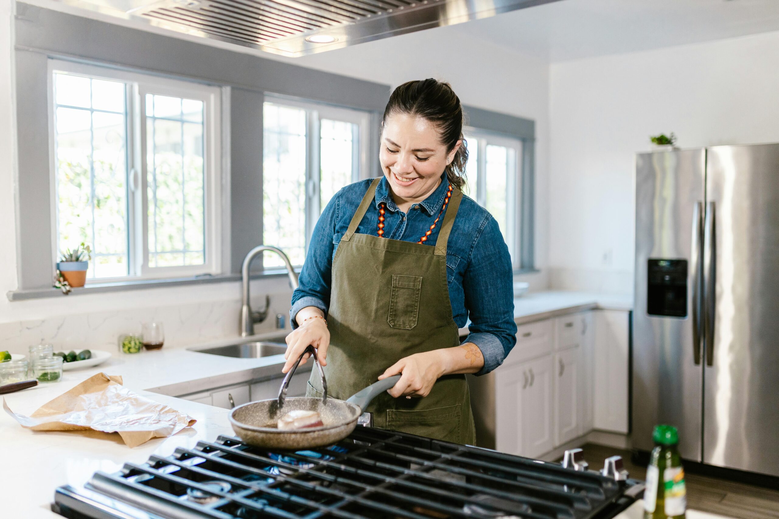 Woman in a cozy kitchen cooking food in a frying pan. Smiling and enjoying the process.